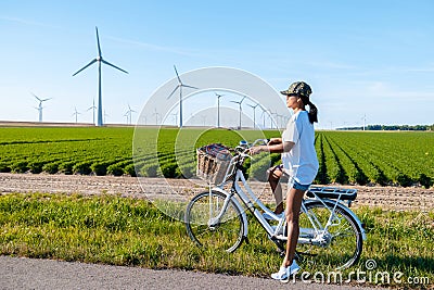 young woman electric green bike bicycle by windmill farm , windmills on a beautiful summer Stock Photo