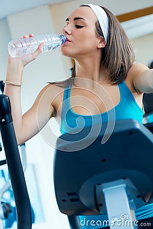 Young woman with elliptic machine drinking water in the gym. Stock Photo