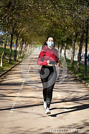 Young woman with face mask because covid, running in the park. Active person outdoors Stock Photo