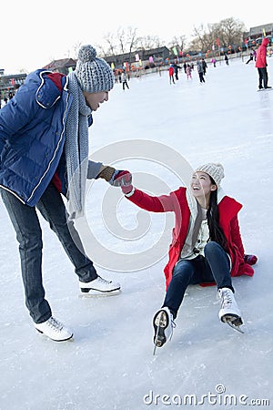Young woman falls on the ice while skating, boyfriend helps her up Stock Photo