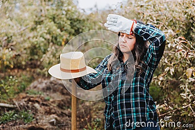 Young latin woman farmer tired from work in the apple plantation, holding a shovel. Woman's occupation. Stock Photo