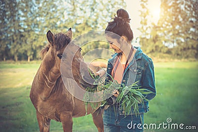 Young woman feeding horse with grass. Asian girl with animal in Stock Photo