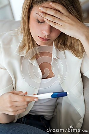 Young woman feeling depressed and sad after looking at pregnancy test result at home. Stock Photo