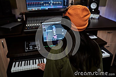 Young woman, female artist looking focused while playing keyboard synthesizer, creating music, sitting in recording Stock Photo