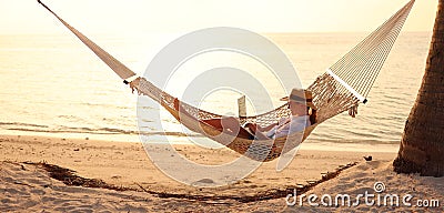 Young woman female freelancer using laptop while lying in hammock on the tropical beach at sunset Stock Photo