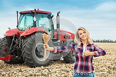 A young woman in a field on a background of a tractor with spike of wheat in her hands Stock Photo