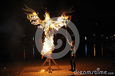 Young woman, the follower of Ukrainian pagan cult, torching the paper scarecrow on the sandy beach of the river Editorial Stock Photo