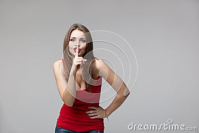 Young woman gesturing for quiet or shushing over grey background Stock Photo