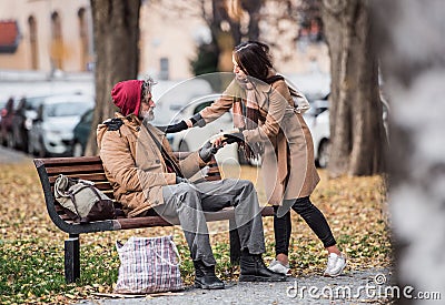 Young woman giving food to homeless beggar man sitting on a bench in city. Stock Photo