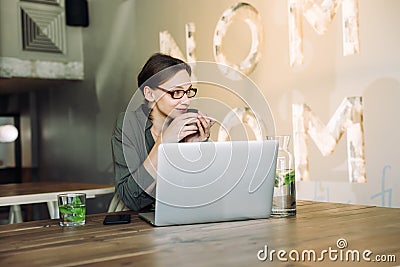 Young woman in glasses with coffee looking away and thinking. Business woman having a coffee and looking out of the window Stock Photo