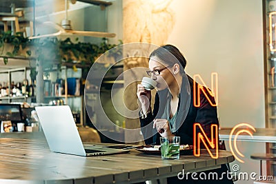 Young woman in glasses with coffee looking away and thinking. Business woman having a coffee and looking out of the window Stock Photo