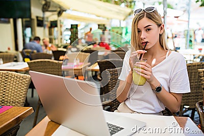 Young woman with glasses on her head smiling joyfully, resting at cafe and browsing internet using laptop computer, sitting at tab Stock Photo
