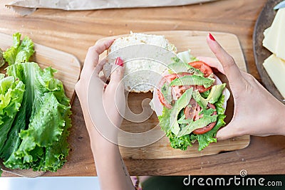 A young woman is going to close a healthy sandwich with lettuce, avocado and tomato at home Stock Photo