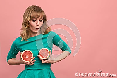 Young woman with grapefruit halves in her hands, cheerful girl in green posing at the camera with grapefruits on a pink Stock Photo