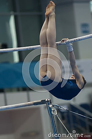 Young woman gymnast hanging on uneven bars at the championship Editorial Stock Photo