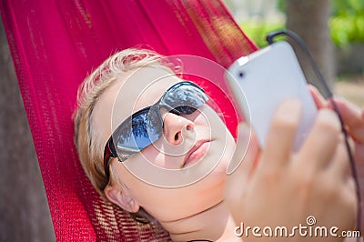 Young woman in hammock under palm trees on ocean beach listen mu Stock Photo