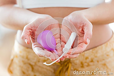 Young woman hands holding different types of feminine hygiene products - menstrual cup and tampons. Stock Photo