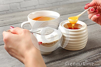 Young woman hands holding spoon of sugar, and honey deciding what to put in tea. Refined vs natural sweetener concept. Stock Photo