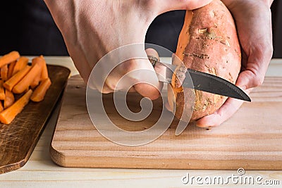 Young woman hands peeling with knife sweet potato, over wooden cutting board, preparing dinner Stock Photo