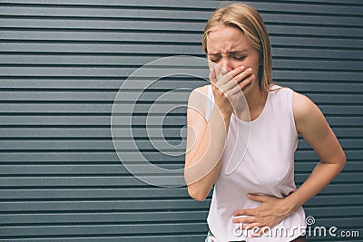 Young woman with hands on stomach having bad aches pain on gray background. Food poisoning, influenza, cramps Stock Photo