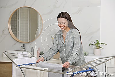 Young woman hanging clean laundry on drying rack in bathroom Stock Photo