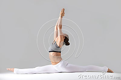 Young woman in Hanumanasana pose, grey studio background Stock Photo