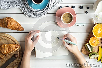Young woman have a breakfast with fresh croissants, coffee and fruits and her hands drawing or writing with ink pen Stock Photo