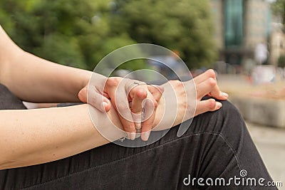 Young woman having rheumatoid arthritis takes a rest sitting on a bench at a park. Hands and legs are deformed. She feels pain. Stock Photo