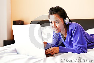 Young woman in headphones using a laptop in bed Stock Photo