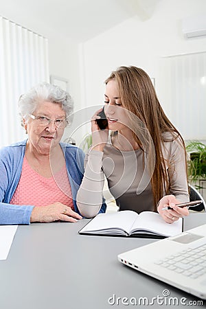 Young woman helping an old senior woman doing paperwork and administrative procedures with laptop computer at home Stock Photo