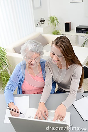 Young woman helping an old senior woman doing paperwork and administrative procedures with laptop computer at home Stock Photo