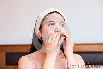 Caucasian girl on her bed, applying moisturizing facial sheet mask. Skin care at home. Stock Photo