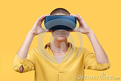 Young woman in her 30s using virtual reality goggles. Woman wearing VR glasses isolated over yellow background. VR experience. Stock Photo