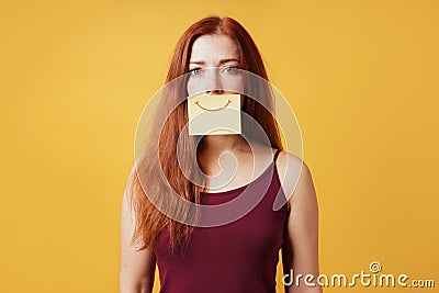 Young woman hiding sadness or depression behind fake smile drawn on paper Stock Photo