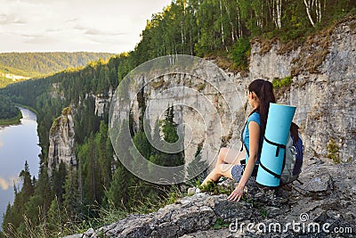 Young woman hiker with backpack sitting on edge of cliff at high altitude Stock Photo