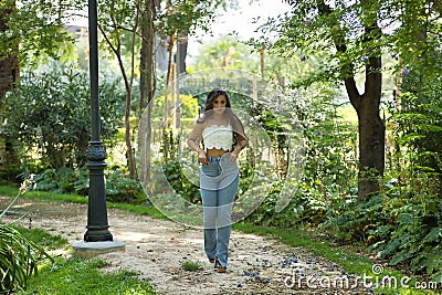 Young woman, Hispanic, beautiful, brunette, with daisy t-shirt and jeans, walking in a park, quiet and lonely. Concept of beauty, Stock Photo