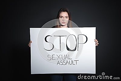 Young woman holding card with words STOP SEXUAL ASSAULT against background Stock Photo