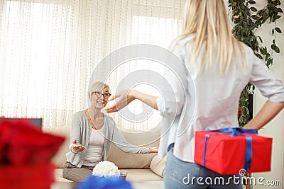 Young woman holding the gift box behind the back for her mother. Cozy living room Stock Photo