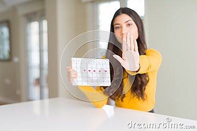 Young woman holding menstruation calendar with open hand doing stop sign with serious and confident expression, defense gesture Stock Photo