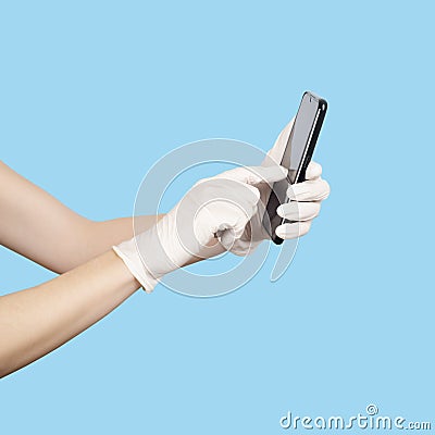 Young woman holding a mobile phone in her hands wearing disposable latex protective gloves isolated on blue Stock Photo
