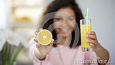 Young woman holding out orange and glass of juice and smiling, rich in vitamins Stock Photo