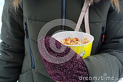 Young woman holding popcorn in winter, in mittens Stock Photo