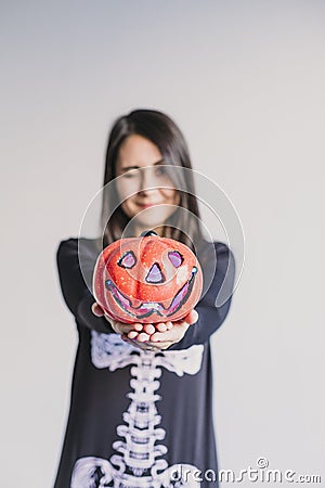 young woman holding a pumpkin and making a wink face. Wearing a black and white skeleton costume. Halloween concept. Indoors. Stock Photo