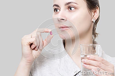 Young woman is holding red vitamin tablet and glass of water. Co Stock Photo
