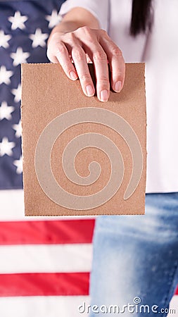 Young woman holds empty cardboard with Space for Text sign against American flag on background. Girl protesting anti-abortion laws Stock Photo