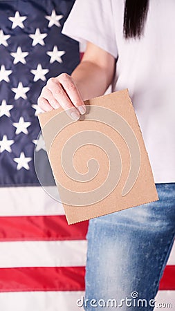Young woman holds empty cardboard with Space for Text sign against American flag on background. Girl protesting anti-abortion laws Stock Photo