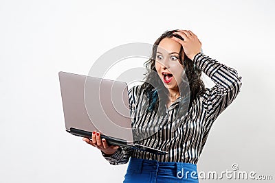 A young woman holds a laptop in her hand, emotionally clutching her head with her hand. on white background Stock Photo