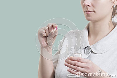 Young woman holds pill and glass of clean water isolated on pistachio background. Health concept. Drug treatment. Take pills. Stock Photo