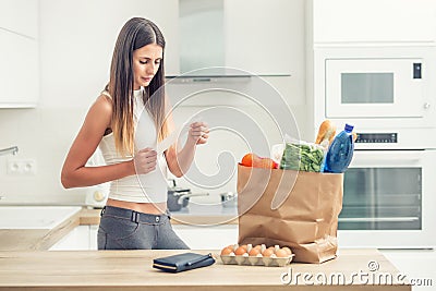 Young woman in home kitchen checks the bill. Purchase on a table in a paper bag Stock Photo