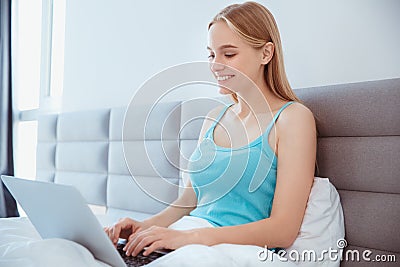 Young woman at home sitting on bed woke up browsing laptop Stock Photo